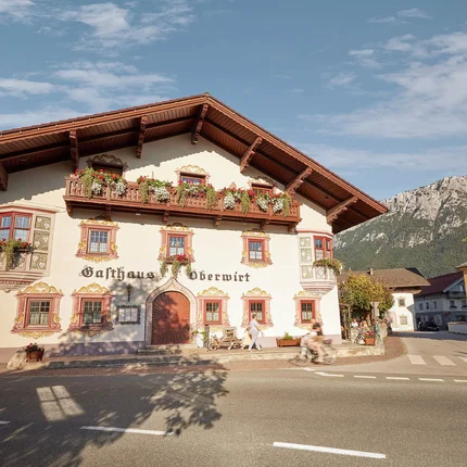 Gasthaus-Hotel Oberwirt © Julian Höck Traditionelles Gasthaus mit Blumen an Fenstern und Balkon in Bergkulisse