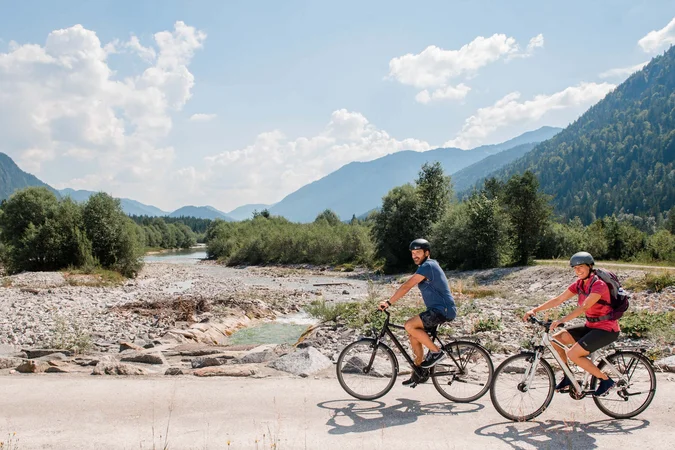 Velontour © Tölzer Land Tourismus - Leonie Lorenz Zwei Radfahrer fahren auf einem Weg neben einem Bach in den Bergen
