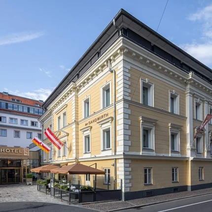 Der Sandwirth © Tinefoto.com - Martin Steinthaler Gelbes Hotelgebäude mit Fahnen und Außenterrasse an sonnigem Tag