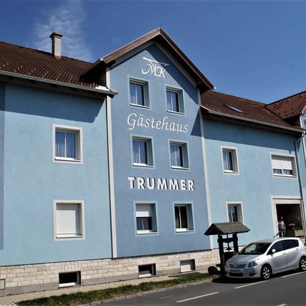 Gasthof & Gästehaus Trummer © Gasthof & Gästehaus Trummer Blaues Gästehaus Trummer mit Autos davor unter blauem Himmel