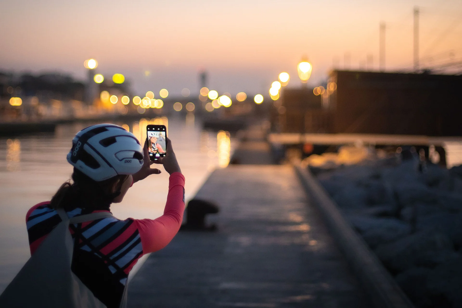 Velontour © Hotel Valverde - MAZ Person mit Helm macht Foto am Wasser bei Sonnenuntergang