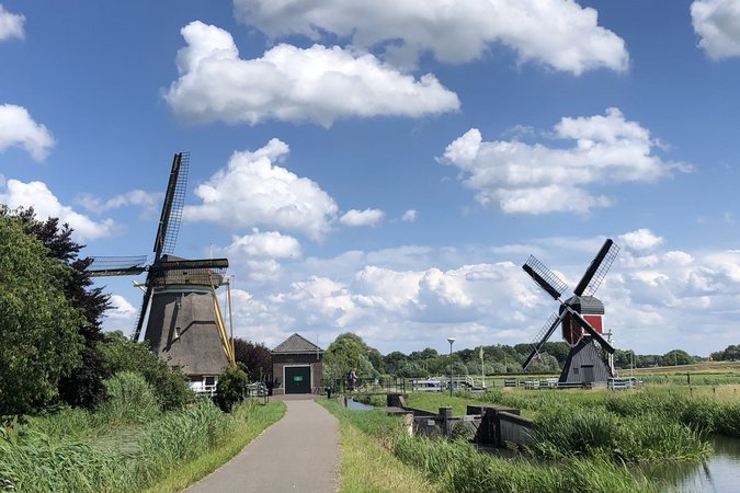Velontour © Boat Bike Tours Weg zu zwei historischen Windmühlen unter einem bewölkten blauen Himmel