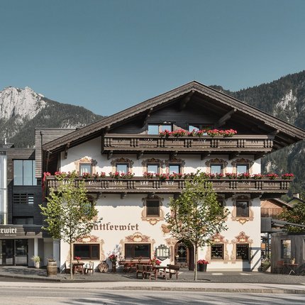 Hotel Sattlerwirt © Alex Gretter Traditionelles Alpenhaus mit Blumendekoration vor Bergen und klarem Himmel