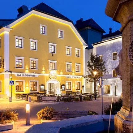 Hotel Gambswirt © Hotel Gambswirt Beleuchtetes gelbes Gebäude neben einem Brunnen bei Nacht in einer Stadt