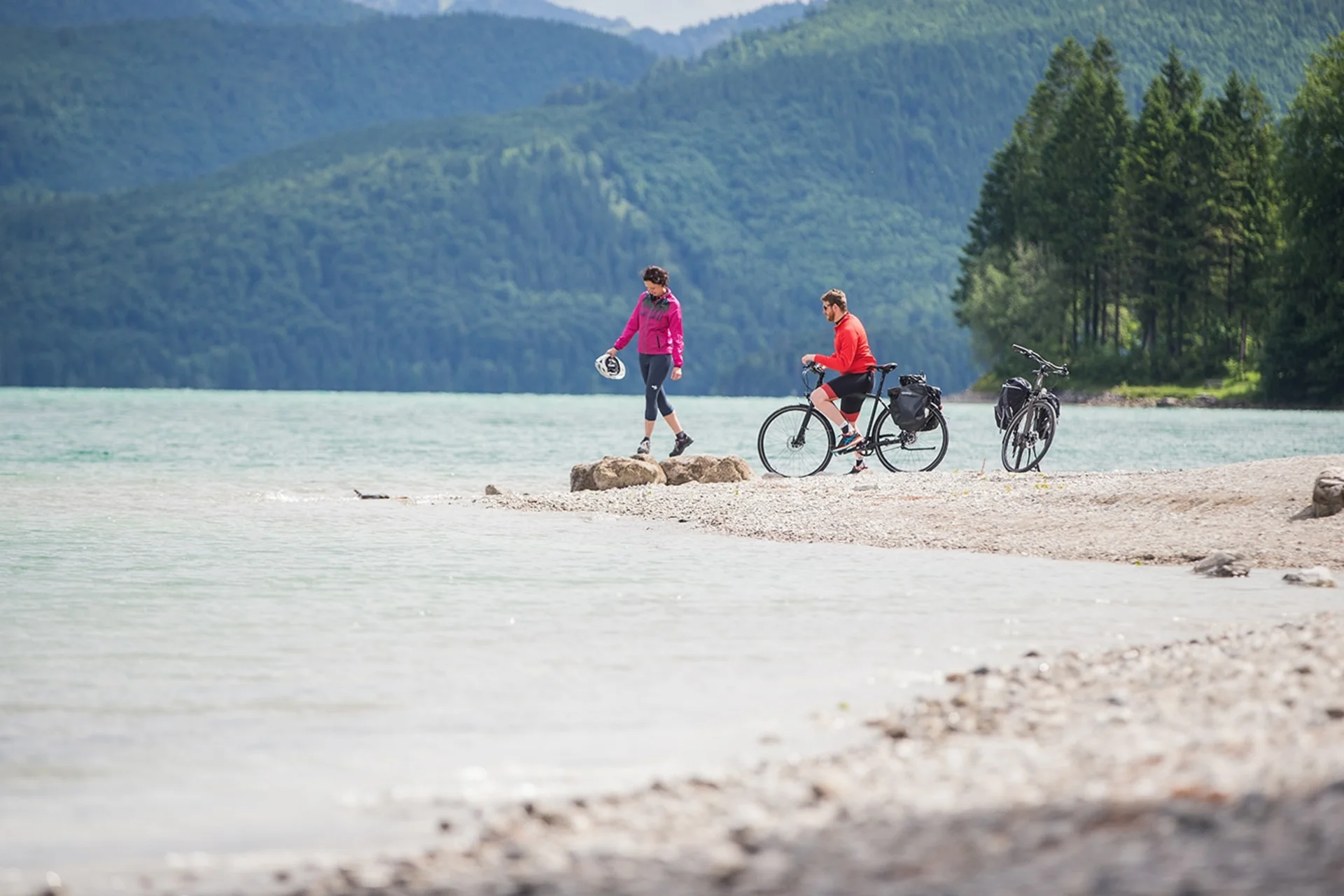 Velontour © Tourismus Oberbayern München e.V. Zwei Radfahrer am Seeufer vor bewaldeten Bergen