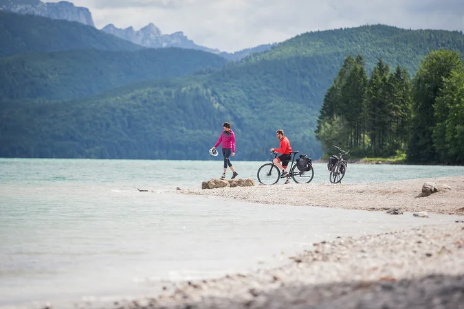 Velontour © Tourismus Oberbayern München e.V. Zwei Radfahrer am Seeufer vor bewaldeten Bergen