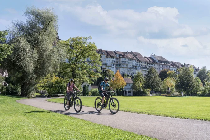Velontour © Beat Belser Zwei Radfahrer auf einem Weg in einem Park vor historischen Gebäuden