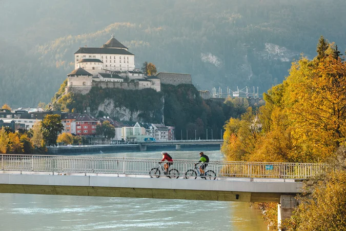 Velontour © Mathäus Gartner Zwei Radfahrer auf einer Brücke mit Burg und herbstlichen Bäumen im Hintergrund