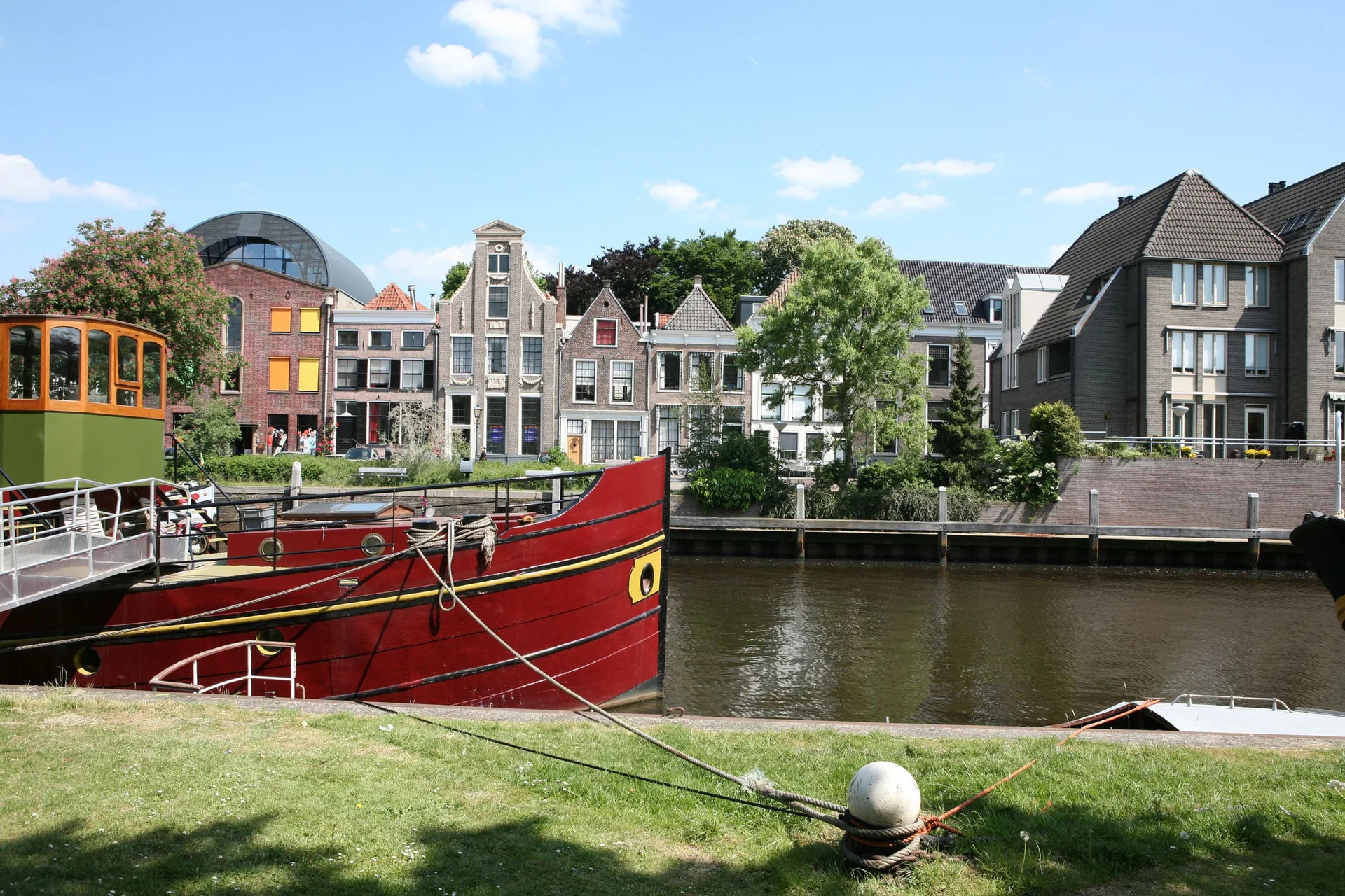 Velontour © Boat Bike Tours Rotes Boot am Flussufer mit historischen Häusern im Hintergrund