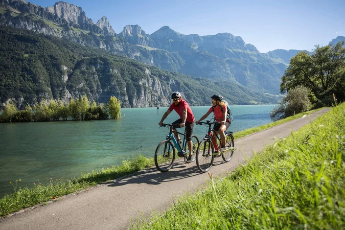 Velontour © Velontour Zwei Radfahrer auf einem Weg neben einem See mit Bergen im Hintergrund