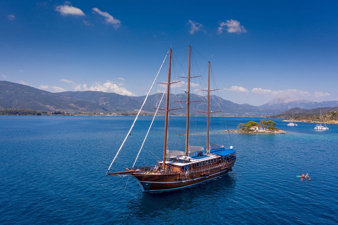 Velontour © Radurlaub Zeitreisen Segelschiff auf blauem Meer vor Insel und Bergen bei klarem Himmel