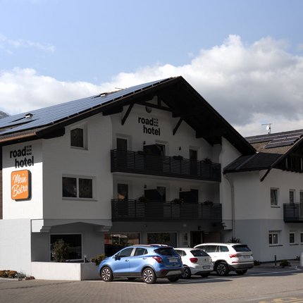 Road Hotel Vinschgau © ueberall GmbH Außenansicht des Road Hotel mit Autos im Vordergrund und Bergen im Hintergrund