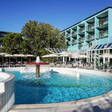 Hotel Savoy © Emanuele Rambaldi Pool mit Springbrunnen und Sonnenschirmen neben blauem Hotelgebäude