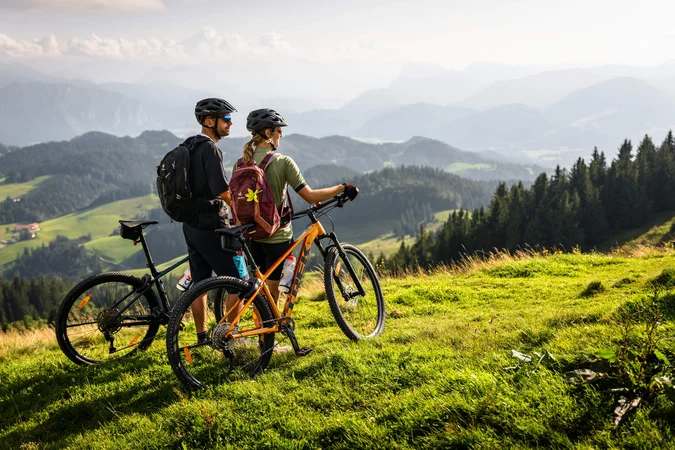 Velontour © Max Dräger Zwei Radfahrer mit Helmen auf Bergwiese mit Blick auf Berge