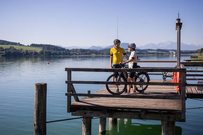 Velontour © Heiko Mandl Zwei Radfahrer auf einem Steg am See mit Bergen im Hintergrund