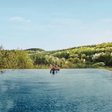 Falkensteiner Balance Resort Stegersbach © Falkensteiner Balance Resort Stegersbach Person entspannt im Infinity-Pool mit Blick auf bewaldete Hügel