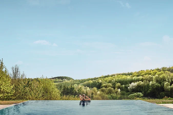 Velontour © Falkensteiner Balance Resort Stegersbach Person entspannt im Infinity-Pool mit Blick auf bewaldete Hügel