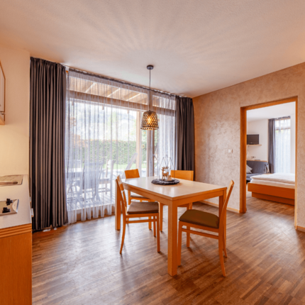Gasthof Residence Brugghof © Gasthof Residence Brugghof Esszimmer mit Holztisch, Stühlen, Küchenecke und Blick ins Schlafzimmer