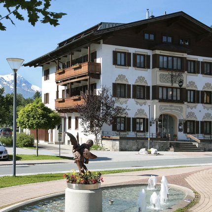 Gasthof Zur Post © Gasthof Zur Post Traditionelles Gasthaus mit Brunnen und Statue vor Alpenkulisse