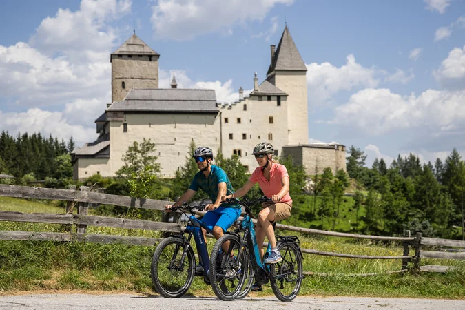 Velontour © Heiko Mandl Zwei Radfahrer vor einer historischen Burg bei sonnigem Wetter