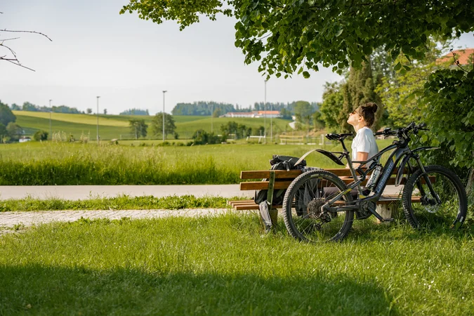 Velontour © Tourismusverein Inn-Salzach Frau auf Parkbank neben Fahrrad genießt sonnige Landschaft
