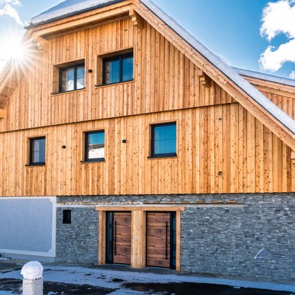 Schitter-Appartements © Schitter Appartements Haus mit Holzfassade und verschneitem Dach bei Sonnenschein