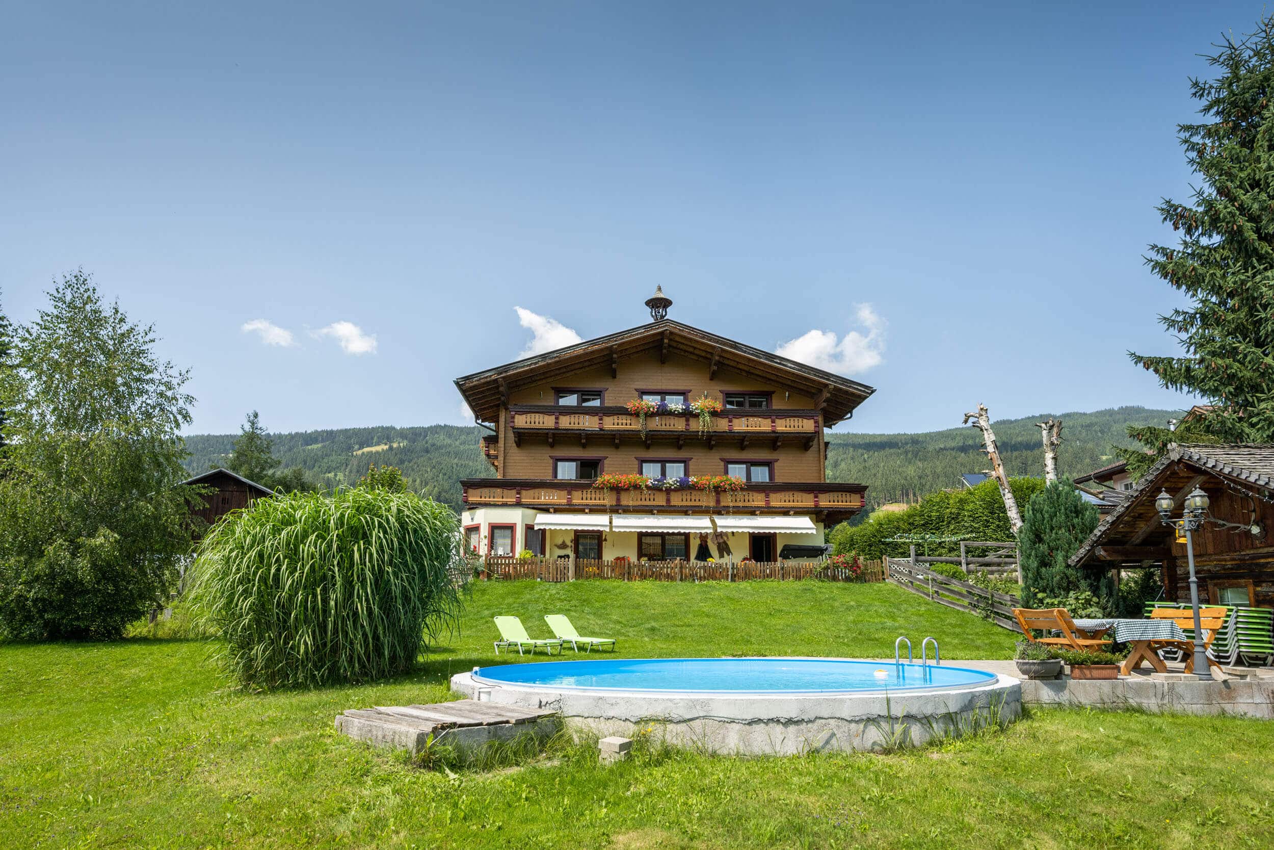 Landhaus Aubauerngut © Lorenz Masser Fotografie Haus mit Balkon, Garten, Pool und Liegestühlen vor bewaldetem Berg